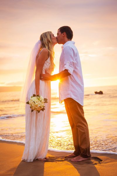 Married couple, bride and groom, kissing at sunset on beautiful tropical beach in Hawaii